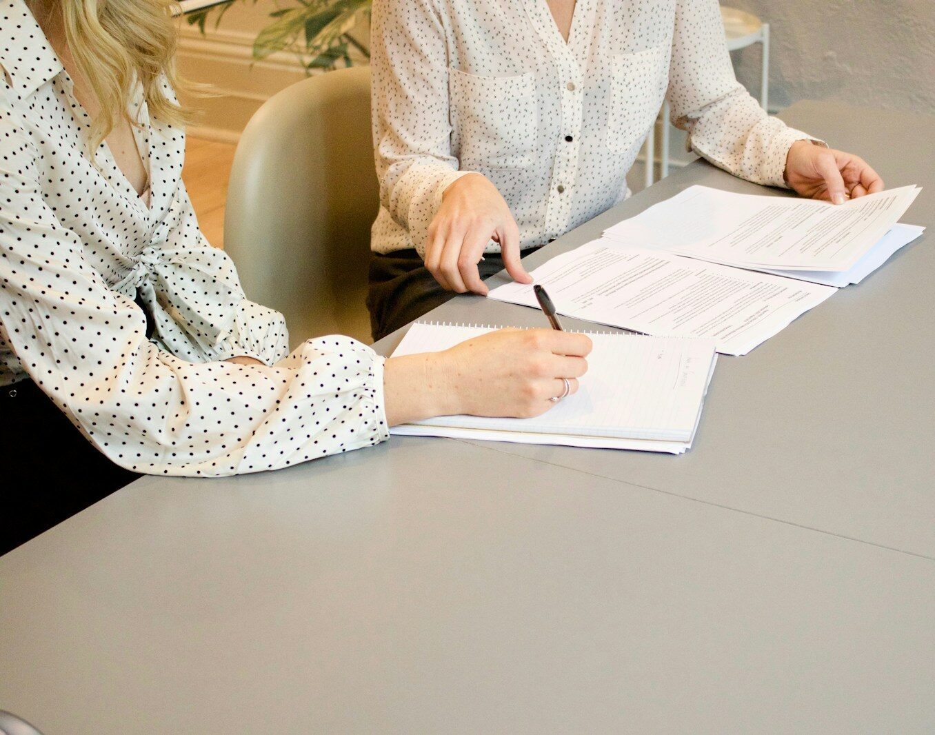 woman signing on white printer paper beside woman about to touch the documents